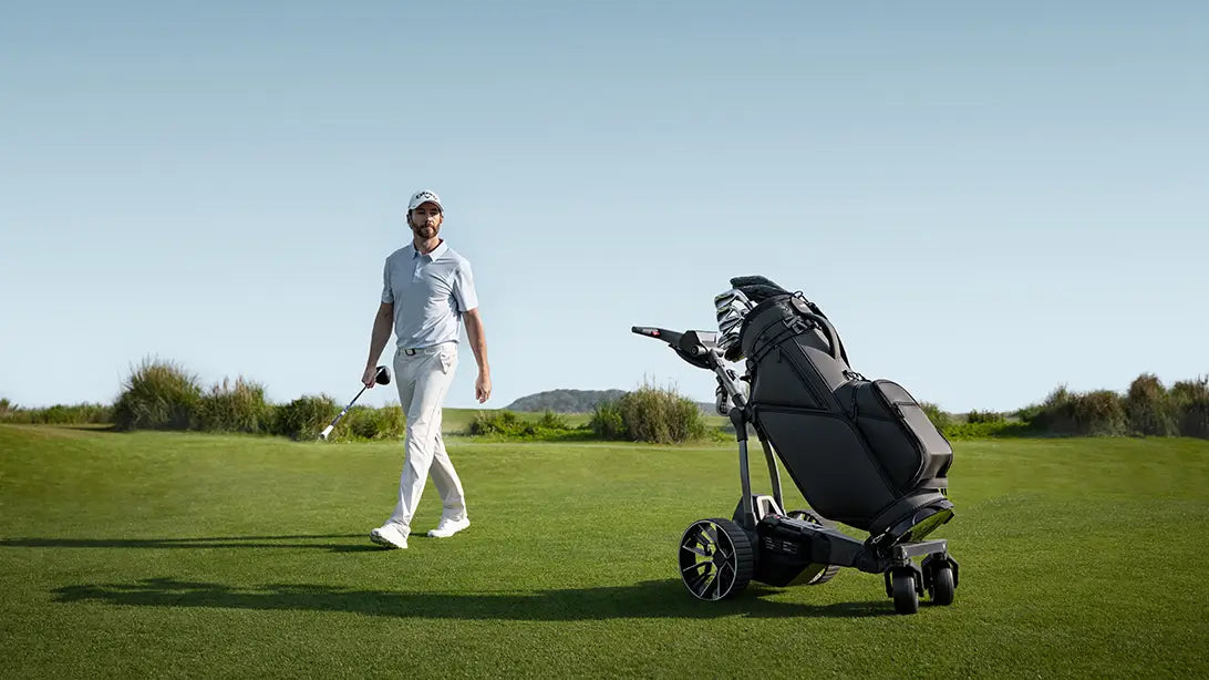 Golfer walking beside an electric golf push cart on a sunny fairway