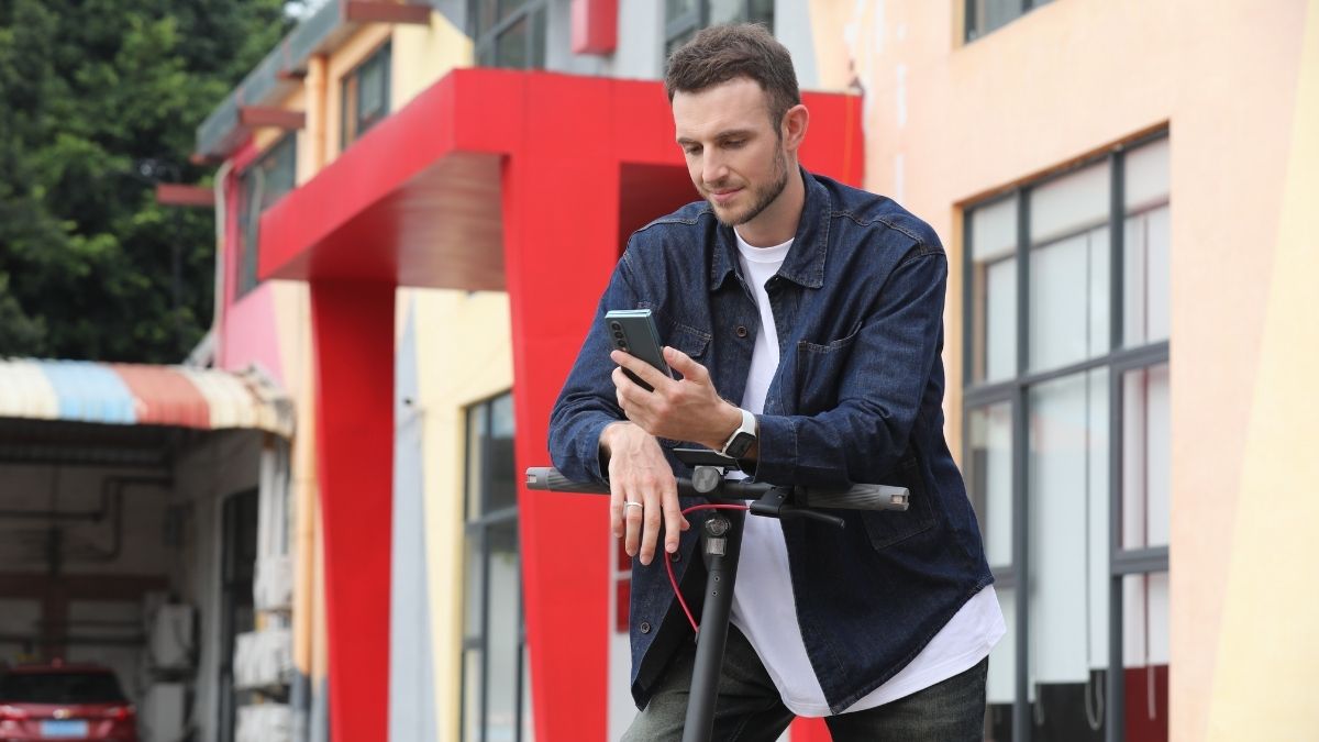 A man leaning on the handlebars of a NAVEE V25 Pro Electric Scooter while using his smartphone.
