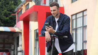 A man leaning on the handlebars of a NAVEE V25 Pro Electric Scooter while using his smartphone.