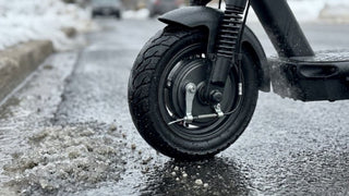 Close-up of a wet electric scooter front wheel on slushy asphalt.